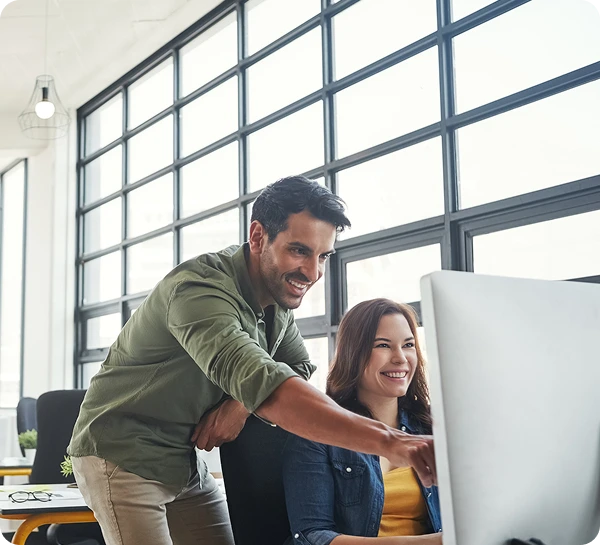 Two colleagues smiling at computer screen.