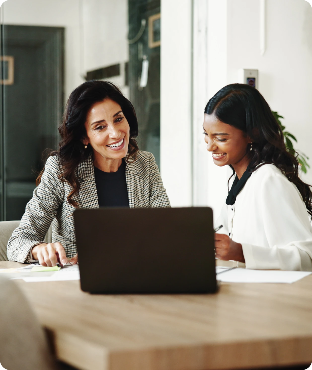 Two women smiling at a laptop screen.